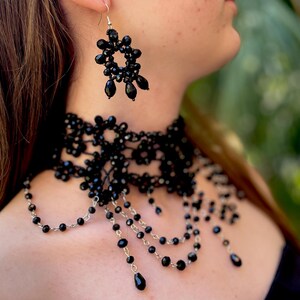 May include: A black beaded choker necklace with a delicate lace design and dangling strands of beads. The necklace is paired with matching black beaded earrings.