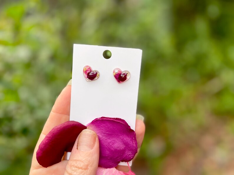 May include: A pair of heart-shaped earrings with pink and red pressed flower petals encased in clear resin.