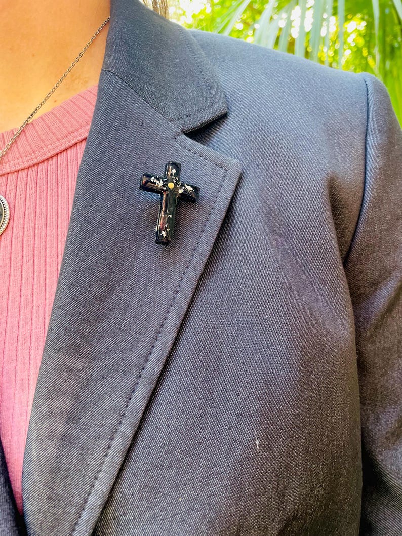 May include: A black blazer with a gold and black cross pin on the lapel.