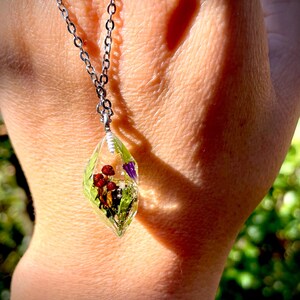 May include: A silver chain necklace with a clear teardrop-shaped pendant containing pressed flowers and red berries.