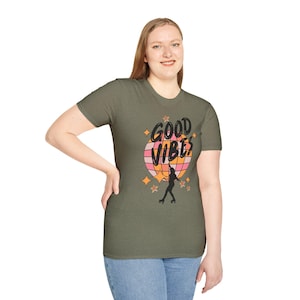 Puede incluir: Una camiseta verde con un gráfico retro de una bola de discoteca y un patinador. El texto "Good Vibes" está impreso en la camiseta.