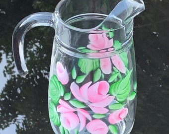 May include: A clear glass pitcher with a painted design of pink roses and green leaves.