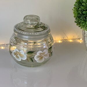 Candy or cookie jar with hand painted white  gold flowers all around with a sealed lid to keep everything fresh.