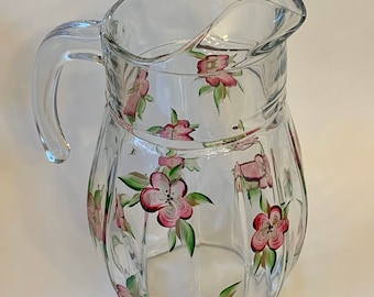 May include: A clear glass pitcher with a handle, decorated with hand-painted pink flowers and green leaves.