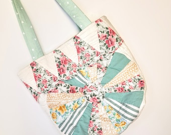 May include: A quilted tote bag featuring a fan-shaped patchwork design in shades of mint green, white, and pink floral patterns. The bag has a single mint green handle with a small white triangle print and a circular center medallion.
