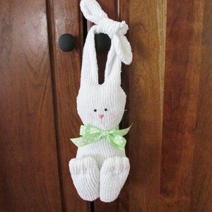 May include: White plush bunny rabbit with green polka dot bow hanging on a wooden door.