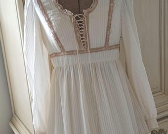 May include: A white maxi dress with a lace trim and a tie-up neckline. The dress has a striped pattern and a tiered skirt.