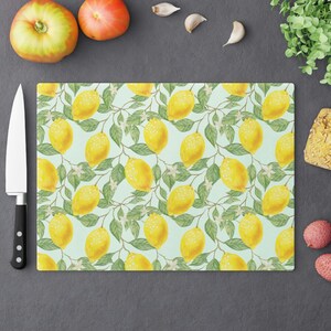May include: A light blue cutting board with a lemon pattern. The board is covered in yellow lemons with green leaves and white flowers.