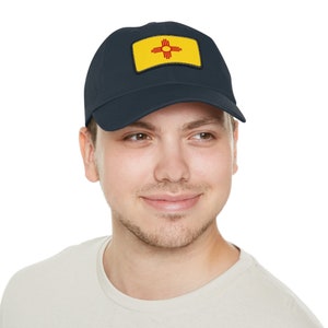 May include: A navy blue baseball cap with a yellow patch featuring the state flag of New Mexico. The flag has a red symbol of the sun with a stylized Zia sun symbol.