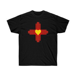 Peut inclure: T-shirt noir avec un symbole de cœur stylisé rouge et jaune, représentant le symbole Zia, un symbole traditionnel du peuple Pueblo du Nouveau-Mexique.