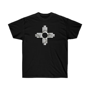 Peut inclure: T-shirt noir avec un graphique blanc vieilli du symbole Zia, un symbole traditionnel du peuple Pueblo du Nouveau-Mexique.