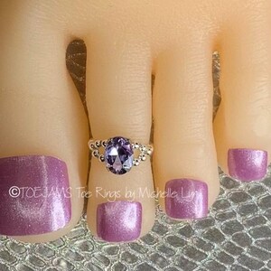 May include: A silver toe ring with a purple oval-shaped gemstone. The ring is on a model's toe with purple nail polish.