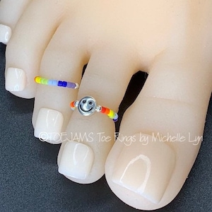 May include: Two toe rings with rainbow colored beads. One ring has a silver smiley face charm.