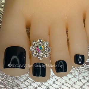 May include: A silver toe ring with a clear rhinestone flower design. The ring is on a toe with black nail polish.