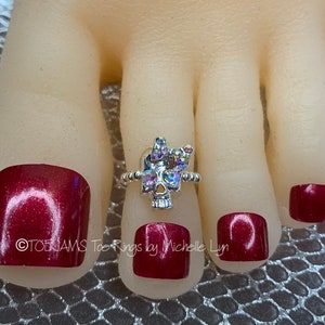 May include: Silver toe ring with a crystal skull design. The ring is on a model's toe with red nail polish. The text "TOE JAMS Toe Rings by Michelle Lyn" is visible in the image.