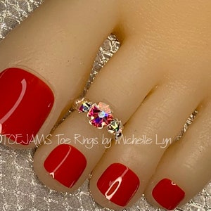 May include: A toe ring with a large iridescent crystal surrounded by smaller crystals. The ring is on a toe with red nail polish.
