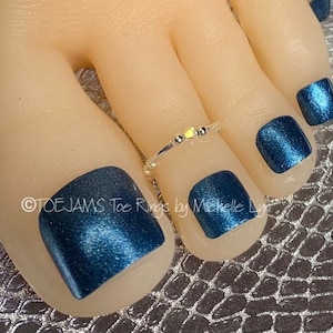 May include: A close-up of a foot with four toes painted a dark blue metallic nail polish. A silver toe ring with small beads is on the second toe.
