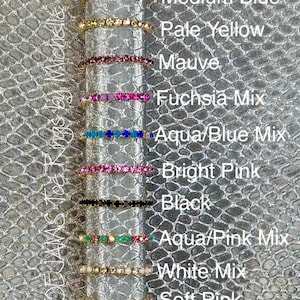 May include: A collection of toe rings in various colors, including multi-colored, medium blue, pale yellow, mauve, fuchsia mix, aqua/blue mix, bright pink, black, aqua/pink mix, white mix, soft pink, and soft pink mix. The rings are displayed on a silver textured background.