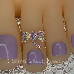 May include: A silver toe ring with a dragonfly design featuring iridescent rhinestones. The ring is on a toe with lavender nail polish.