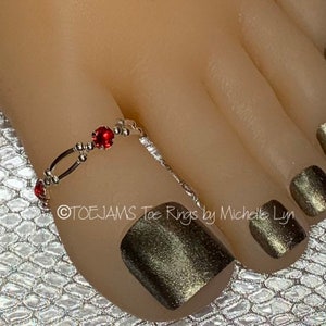 May include: Silver toe ring with a single red rhinestone. The ring is on a foot with gold nail polish.