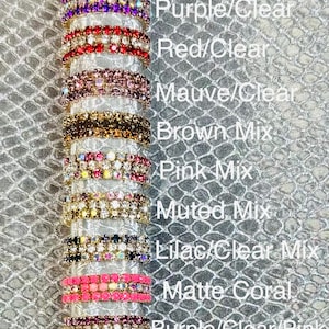 May include: A display of various rhinestone bracelets in different color combinations, including Ocean Mix, Tuxedo Mix, and Matte Coral. The text on the image lists the color names. The bracelets are stacked on a silver-colored cylindrical object.