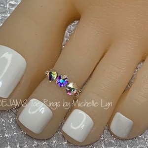 May include: A toe ring with three iridescent gemstones. The ring is worn on a foot with white nail polish. The text "TOEJAMS Toe Rings by Michelle Lyn" is visible.