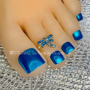 May include: Blue toe rings with a dragonfly design. The rings are made of metal and have blue rhinestones. The toe rings are on a model's foot with blue nail polish.