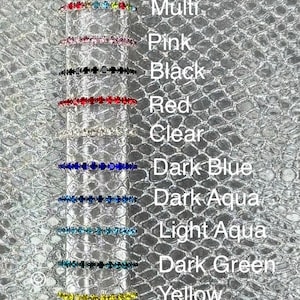 May include: A collection of colorful, thin rings with various gemstone colors, including multi-colored, pink, black, red, clear, dark blue, dark aqua, light aqua, dark green, and yellow. The rings are displayed against a textured silver background.