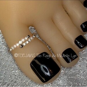 May include: A silver-toned bypass toe ring featuring a row of small, clear, round-cut stones along the band. The ring is worn on a toe with black nail polish. The text "©TOEJAMS Toe Rings by Michelle Lyn" is printed across the image.