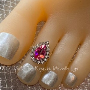 May include: Close-up of a foot with silver nail polish and a pink and silver toe ring. The toe ring is a teardrop shape with a pink center stone and a silver border. The text "TOEJAMS Toe Rings by Michelle Lyn" is visible.