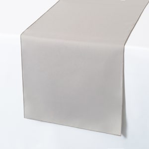 May include: A light gray table runner with a brown border. The runner is made of a smooth fabric and has a subtle sheen.