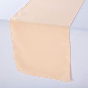 May include: A peach-colored satin table runner. The runner is smooth and has a subtle sheen.