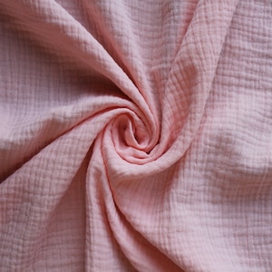 May include: A close-up of a soft, pink, textured fabric. The fabric is folded and twisted, creating a swirling pattern.