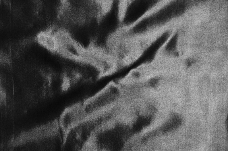 May include: A close-up of a black fabric with a smooth, silky texture. The fabric is wrinkled and folded, creating a dramatic and abstract pattern.