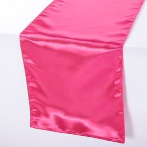 May include: A bright pink satin table runner. The runner is smooth and has a slight sheen.