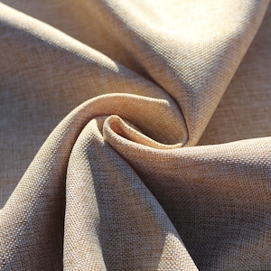May include: Close-up of a beige fabric with a textured weave. The fabric is folded and twisted, creating a swirling pattern.