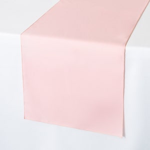 May include: A light pink table runner. The runner is made of a smooth, silky fabric and is perfect for adding a touch of elegance to any table setting.