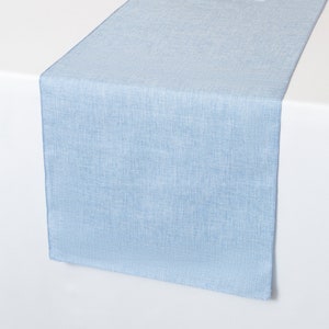 May include: A light blue table runner with a subtle textured pattern. The runner is laid out on a white surface.