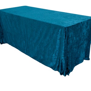 May include: A teal blue rectangular tablecloth with a textured, crushed velvet finish. The tablecloth is draped over a table and has a slight sheen.