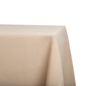 May include: A close-up of a beige tablecloth with a smooth, even texture. The tablecloth is draped over a table, with the edges of the tablecloth hanging down the sides.