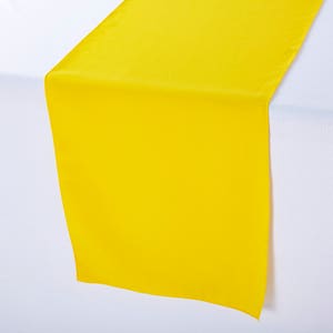 Peut inclure: Un chemin de table jaune vif en satin. Le chemin de table est posé à plat sur une surface blanche.