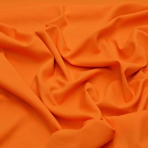 May include: A close-up of a bright orange fabric with soft folds and wrinkles. The fabric has a smooth, even texture.