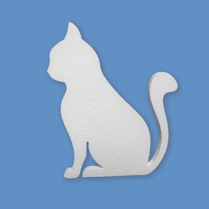 May include: White paper cutout of a cat sitting with its tail curled around its body. The cat is facing to the left.