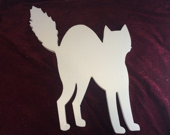 May include: White foam cutout of a cat in a crouching position. The cat is facing to the right, with its tail curled around its body.