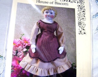 May include: A pattern for an 18-inch china doll body and dress. The doll is wearing a red and white plaid dress with a brown ruffled skirt. The pattern is from House of Biscotti.