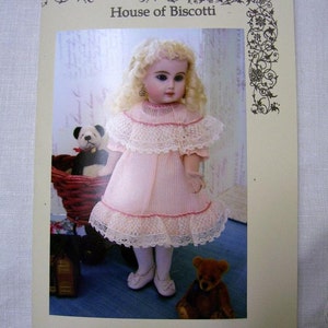May include: A pattern for an 8-inch petite doll simple wardrobe. The pattern is from House of Biscotti. The image shows a doll wearing a pink dress with lace trim and a teddy bear.