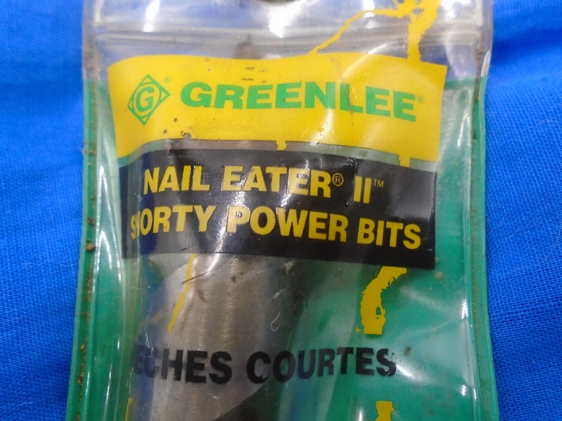 Puede incluir: Un primer plano de un paquete que contiene una broca Greenlee Nail Eater II Shorty Power Bits. El paquete es amarillo y verde con el texto "Greenlee", "Nail Eater II", "Shorty Power Bits" y "Inches Courtes".