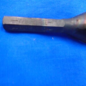 Puede incluir: Primer plano de una herramienta de metal plateado con cabeza hexagonal. La herramienta tiene un mango negro y est&aacute; ligeramente curvada.