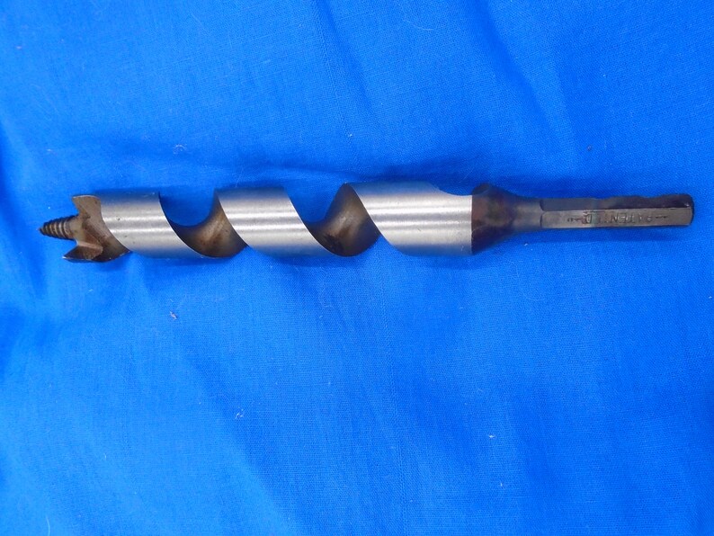 Puede incluir: Una broca de taladro plateada con un dise&ntilde;o de torsi&oacute;n. La broca mide aproximadamente 25 cm de largo y tiene un mango negro.