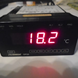 May include: Black OMEGA DP20 digital temperature controller displaying 18.2 degrees Celsius. The device has buttons labeled MAX, MIN, HOLD, AL1, AL2, RNG, DISP, ALM, RNG, SET, and arrow keys. The temperature is shown in bright red digits.